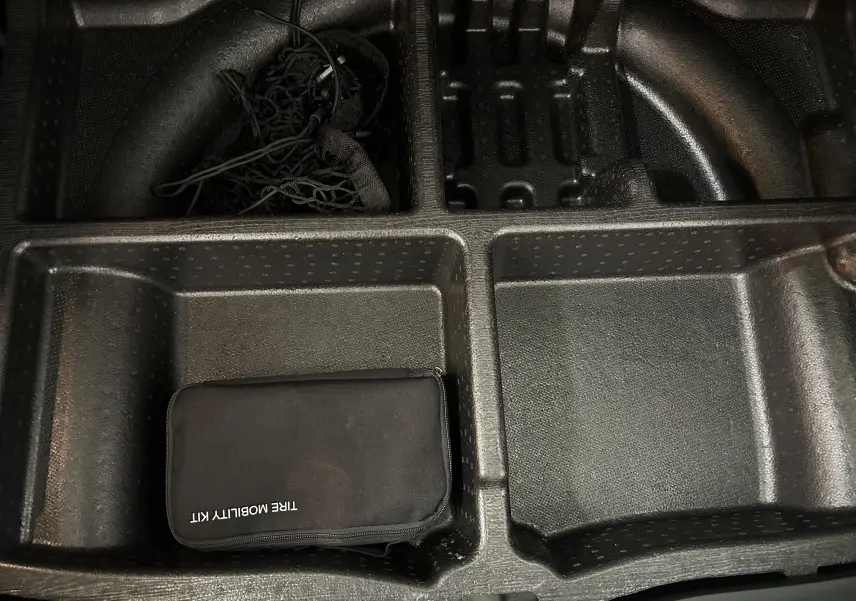 Rangement sous coffre du Hyundai Tucson gris, montrant un kit de mobilité pneu noir dans un compartiment en plastique.