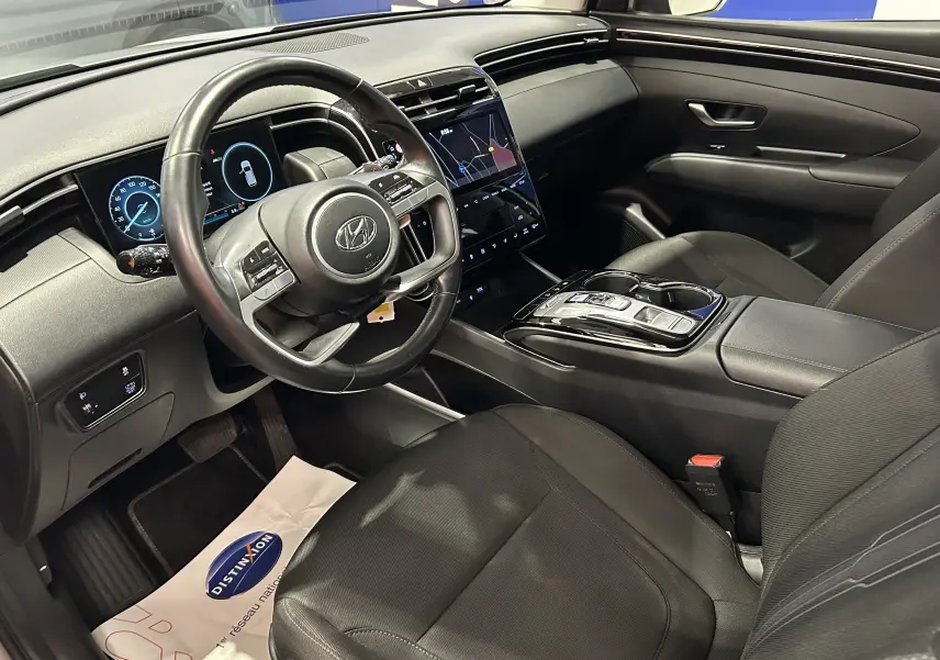 Vue intérieure côté conducteur du Hyundai Tucson Hybrid 2022 avec tableau de bord numérique et sellerie noire tissu et cuir.