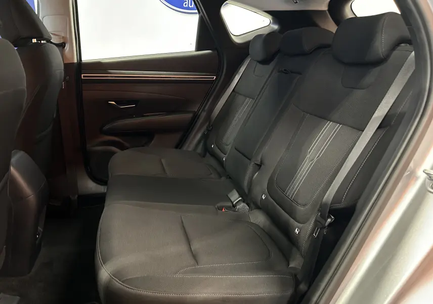 Vue latérale intérieure des sièges arrière noirs en tissu du Hyundai Tucson gris, avec ceinture de sécurité et porte côté gauche visible.