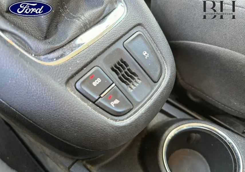 Gros plan sur la console centrale noire avec boutons Eco et aide au stationnement, volant cuir partiel visible.