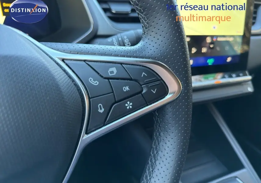 Gros plan sur le volant en cuir perforé avec commandes intégrées du Renault Symbioz gris Rafale, tableau de bord numérique en arrière-plan.