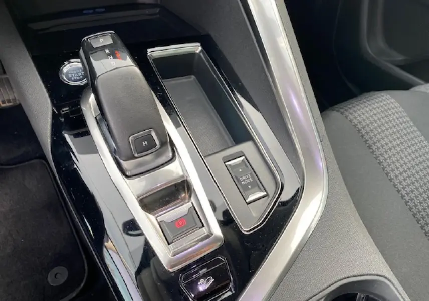 Gros plan sur la console centrale noire brillante du Peugeot 3008 2021, avec levier de vitesse automatique et bouton Drive Mode.