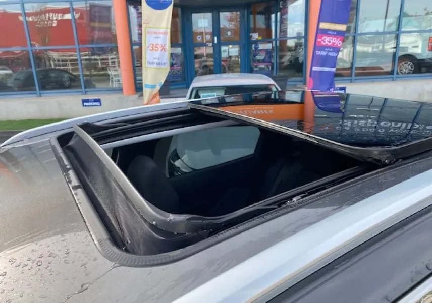 Toit ouvrant panoramique ouvert vu en gros plan sur un Peugeot 3008 gris platinium stationné devant une vitrine.