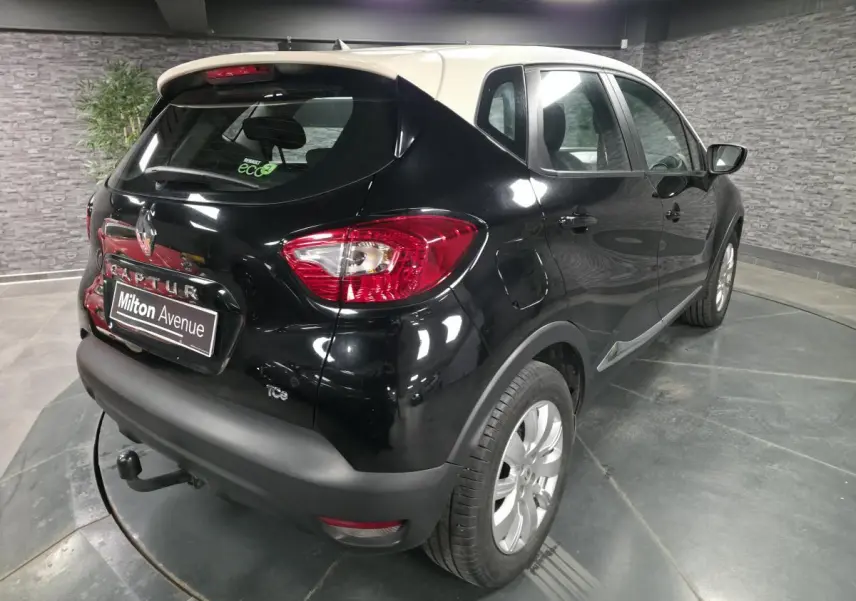 Vue 3/4 arrière droite d'un Renault Captur noir avec toit blanc, attelage et jantes alliage 16 pouces dans un garage.