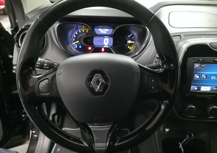 Vue rapprochée du volant noir brillant de la Renault Captur 2014 avec tableau de bord et écran multimédia allumés.