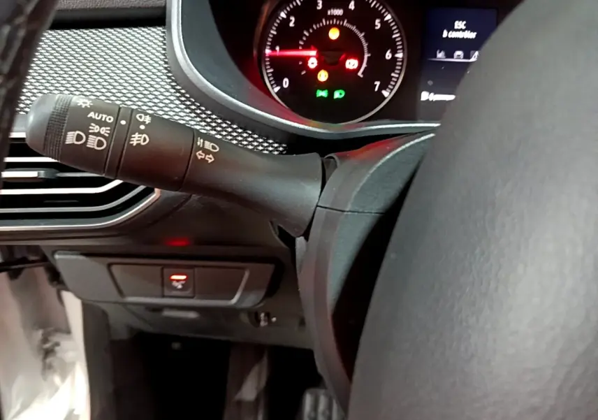 Gros plan intérieur sur le volant cuir synthétique et la commande des phares de la Dacia Sandero Confort TCe 90 blanche.