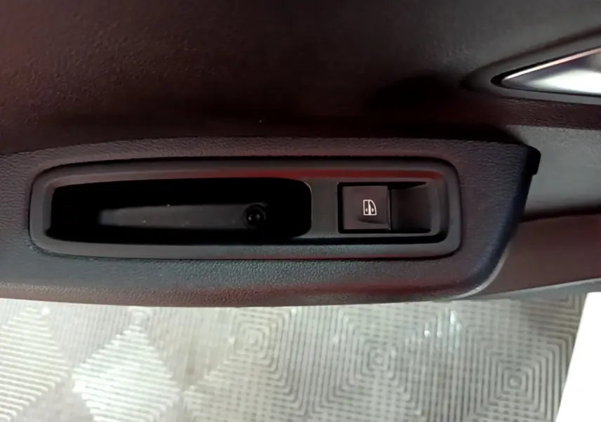 Gros plan sur la commande de lève-vitre côté conducteur de la Dacia Sandero Confort blanche, intérieur noir.