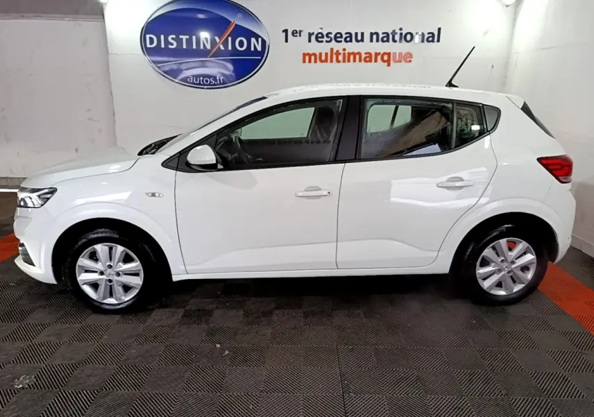 Vue de profil côté gauche d'une Dacia Sandero blanche 2022, finition Confort, dans un showroom intérieur.