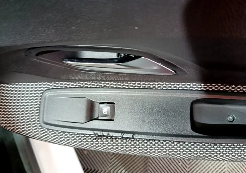 Gros plan sur la commande de lève-vitre côté conducteur d'une Dacia Sandero blanc, avec poignée de porte noire.