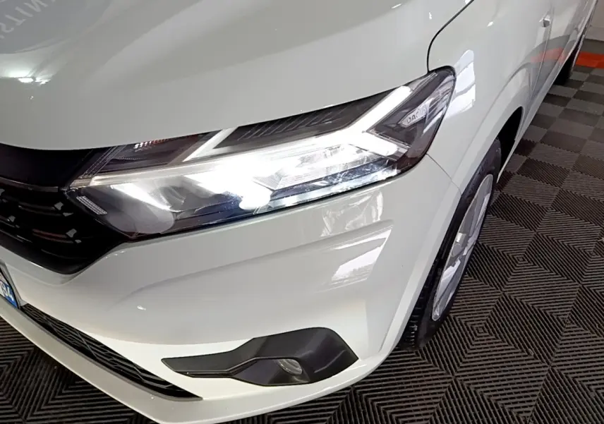 Gros plan sur l'avant droit blanc d'une Dacia Sandero 2022 avec phares LED allumés et antibrouillards visibles.