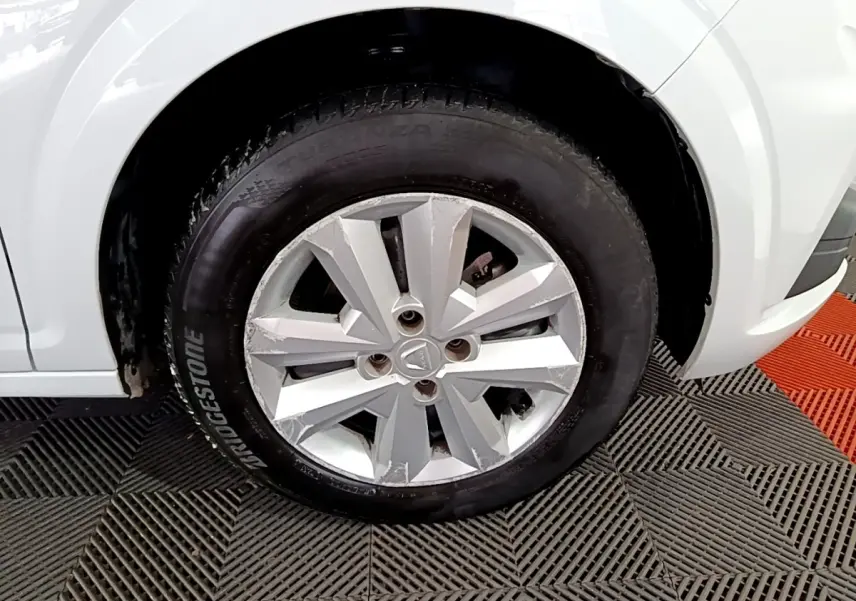 Gros plan sur la roue avant gauche d'une Dacia Sandero blanche, jante en alliage argentée avec pneus Bridgestone.