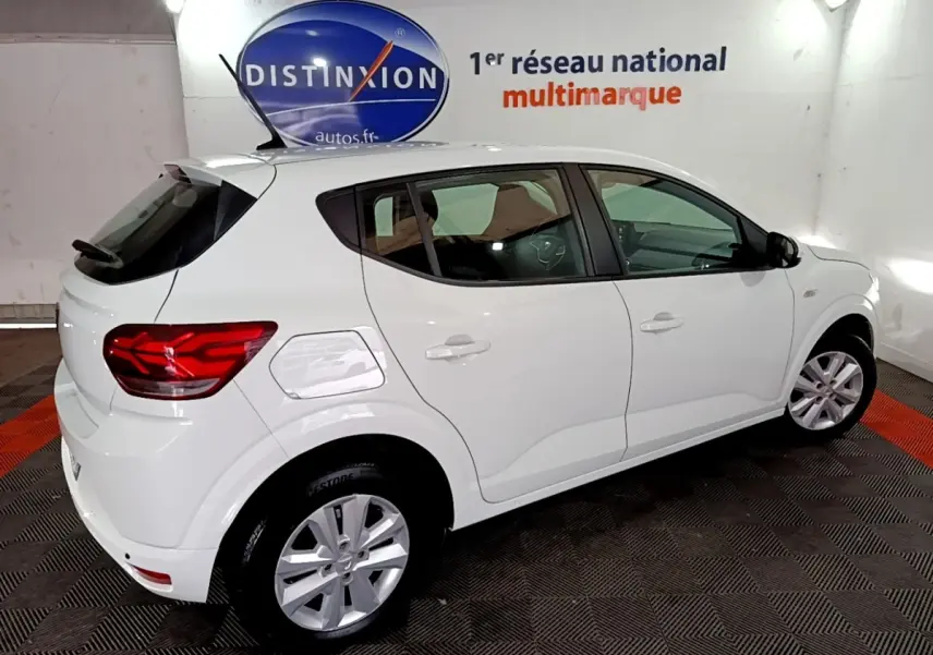 Vue 3/4 arrière droite d'une Dacia Sandero blanche 2022 dans un showroom avec logo Distinxion en arrière-plan.