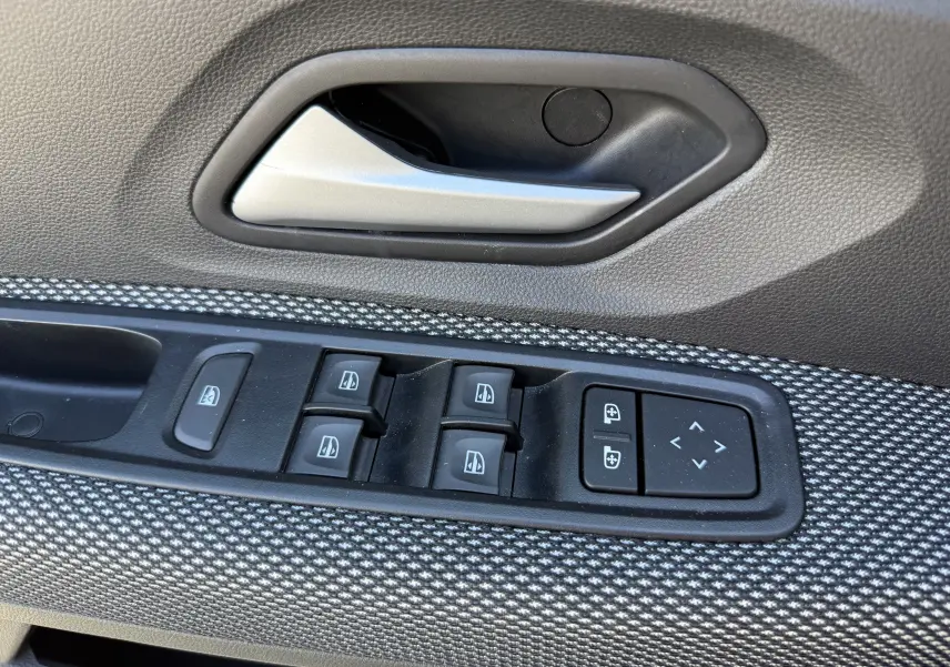 Gros plan sur la commande des vitres électriques et la poignée intérieure côté conducteur du Dacia Sandero Stepway 2025, finition tissu gris.