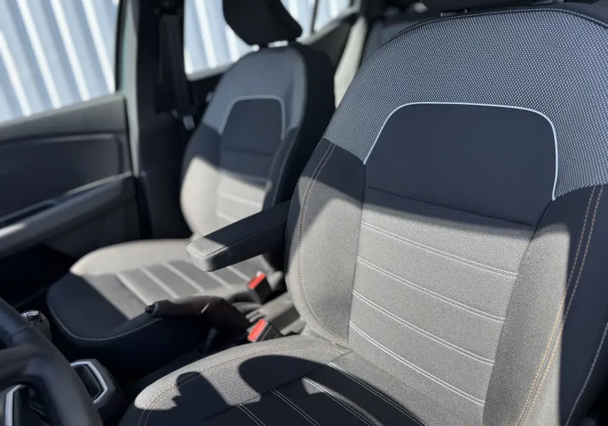Gros plan sur les sièges avant gris et noirs du Dacia Sandero Stepway, mettant en valeur l'accoudoir central et les surpiqûres contrastées.