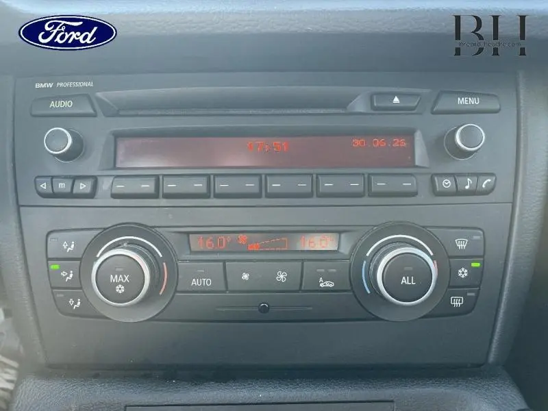 Vue rapprochée du tableau de bord BMW X1 sDrive18dA 2011 avec commandes climatisation bi-zone et autoradio intégré.