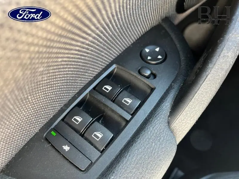 Commande des vitres électriques côté conducteur en plastique noir avec tissu gris, vue rapprochée intérieure du véhicule.