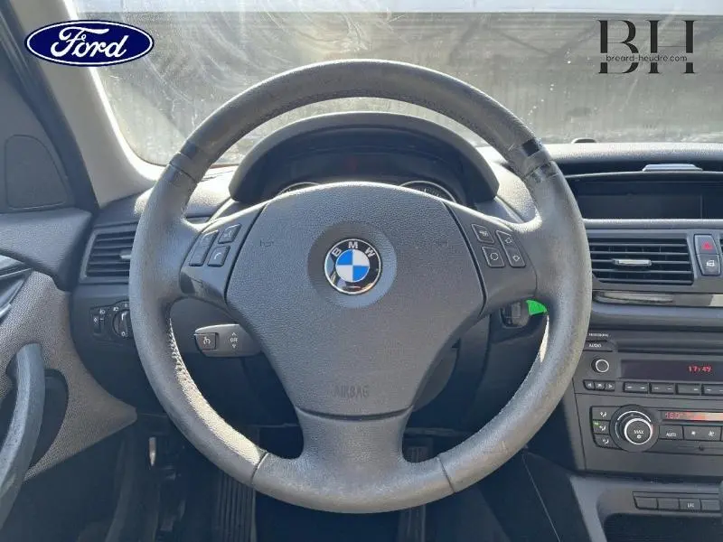 Vue centrée sur le volant cuir multifonction d'une BMW X1 gris, avec tableau de bord et console centrale visibles.