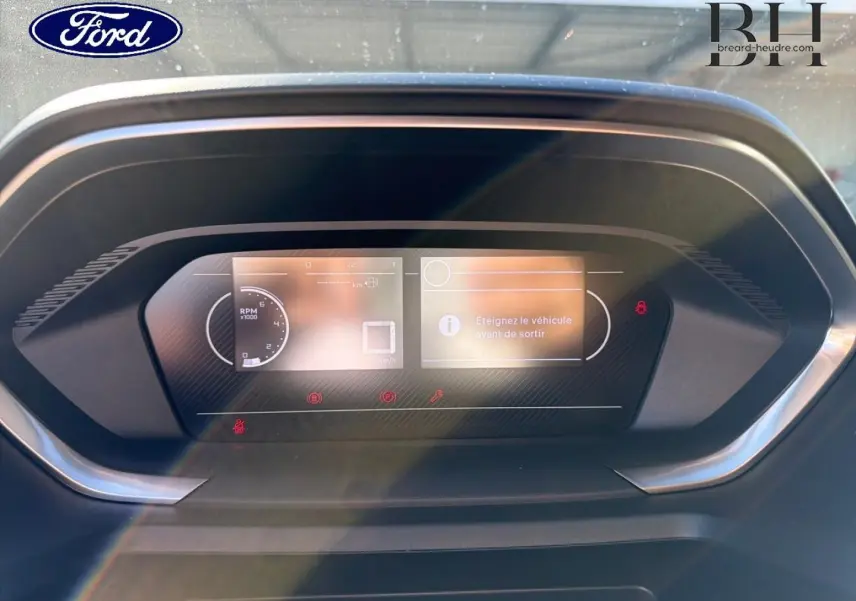 Affichage numérique du tableau de bord d'un Peugeot Partner 2025, avec message d'alerte et éclairage ambiant.
