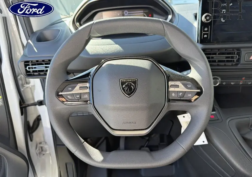 Vue intérieure centrée sur le volant Peugeot noir avec logo lion, tableau de bord et écran tactile en arrière-plan.