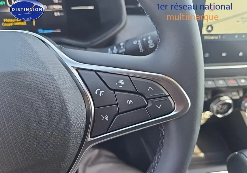 Gros plan sur les commandes multifonctions côté droit du volant de la Renault Clio V bleu iron, avec écran tactile en arrière-plan.