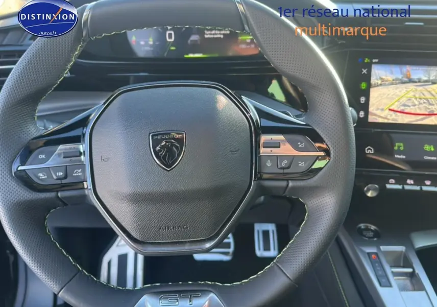 Vue rapprochée du volant cuir noir à surpiqûres vertes de la Peugeot 408 Hybrid 145 GT avec tableau de bord numérique et écran tactile.