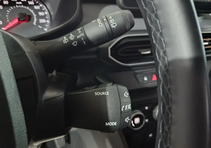 Gros plan sur la commande multifonctions du volant cuir synthétique de la Dacia Sandero Extreme+ bleu, tableau de bord en arrière-plan.
