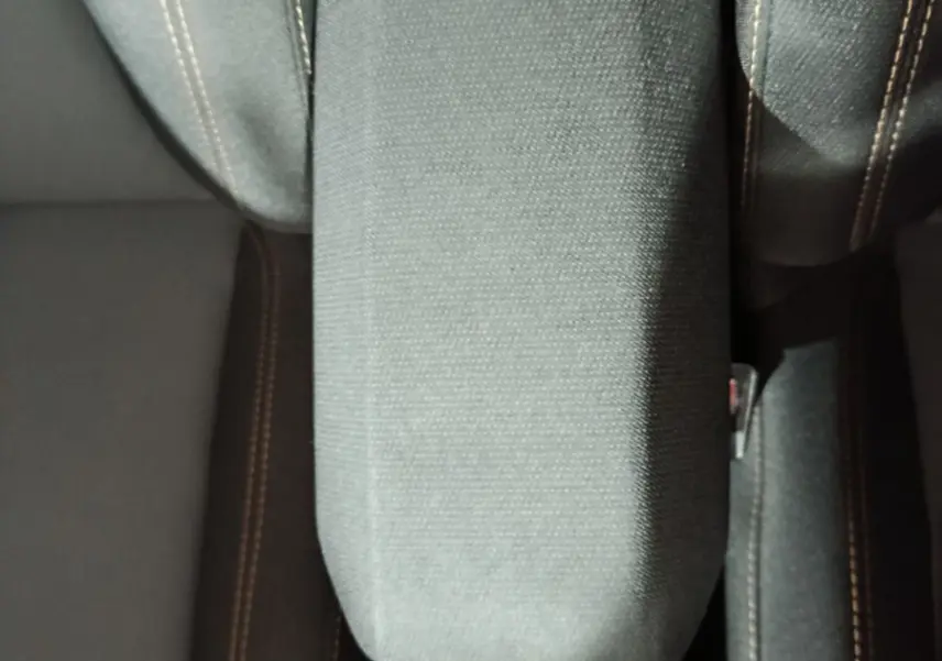 Vue rapprochée de l'accoudoir central tissu gris et des sièges avant noirs avec surpiqûres contrastantes dans une Dacia Sandero 2024.