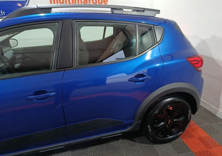 Vue côté droit arrière d'une Dacia Sandero Extreme+ TCe 110 2024 bleu avec jantes noires et logo Stepway sur le montant arrière.