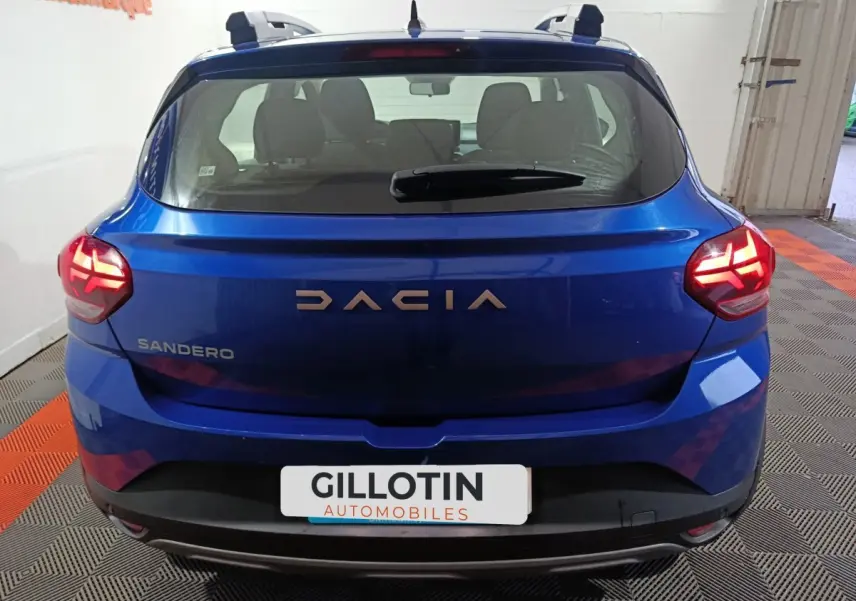 Vue arrière d'une Dacia Sandero bleu intense avec feux LED allumés dans un garage.