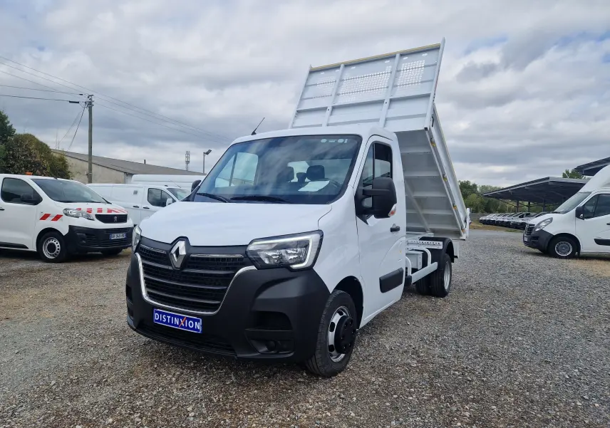 Renault Master Benne blanc vu en 3/4 avant droit, benne relevée et roues jumelées visibles sur terrain gravillonné.