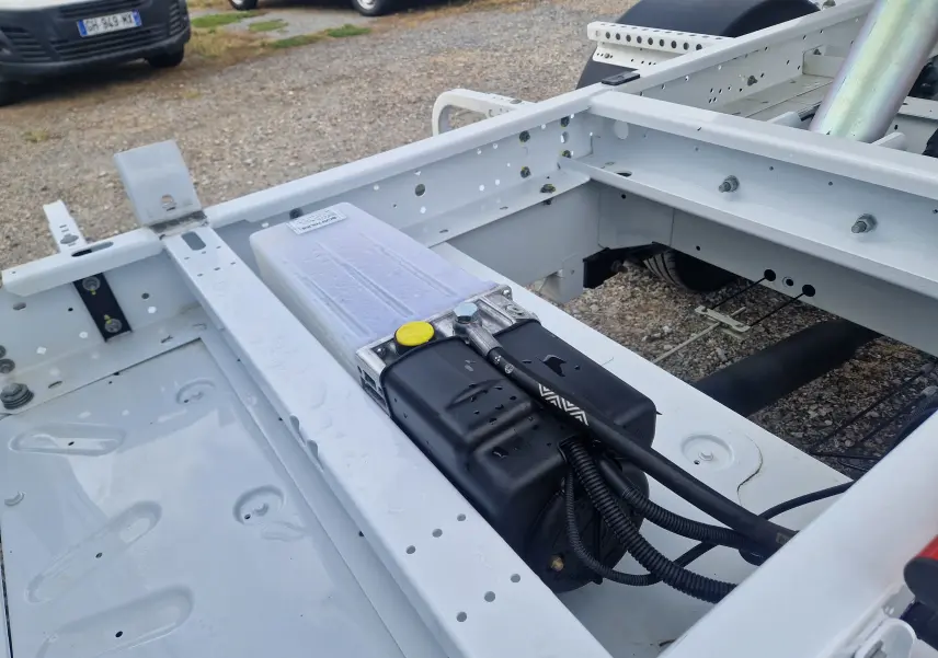 Vue rapprochée du châssis blanc du Renault Master Benne L2 avec composants hydrauliques et roues jumelées visibles.