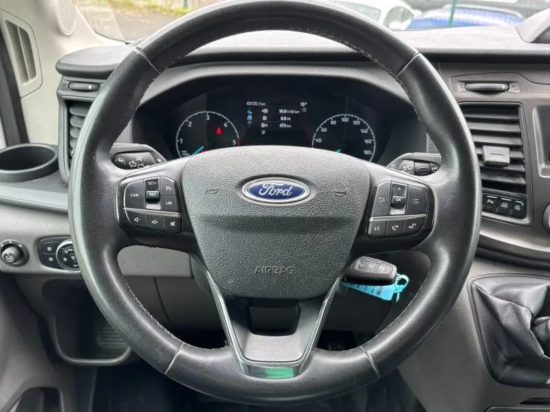 Vue rapprochée du volant cuir multifonction du Ford Transit Fourgon blanc, avec tableau de bord et commandes visibles.