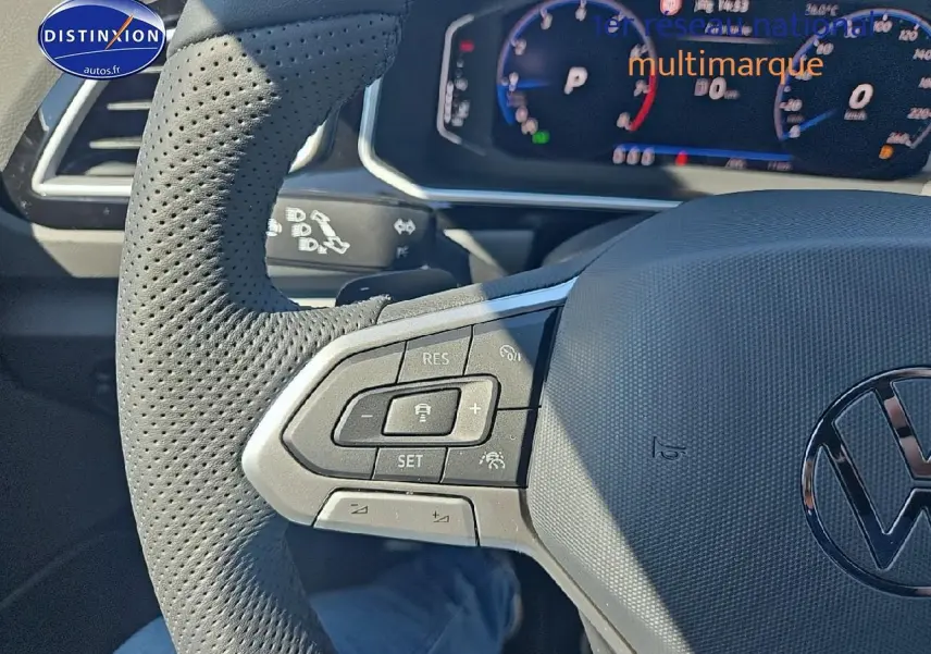 Gros plan sur le volant cuir perforé du Volkswagen T-Roc noir perle, avec commandes multifonctions et cockpit numérique en arrière-plan.