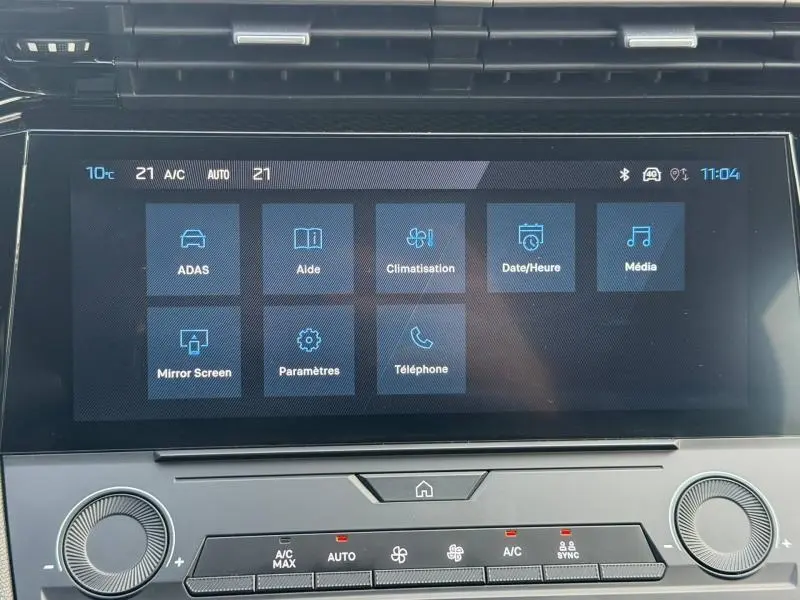 Écran tactile central de la Peugeot 308 2024 blanc Okénite, affichant le menu principal avec options de climatisation et média.