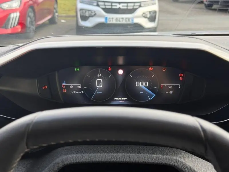 Tableau de bord numérique de Peugeot 308 2024 vu de face depuis le volant, avec affichage du compte-tours et vitesse à zéro.