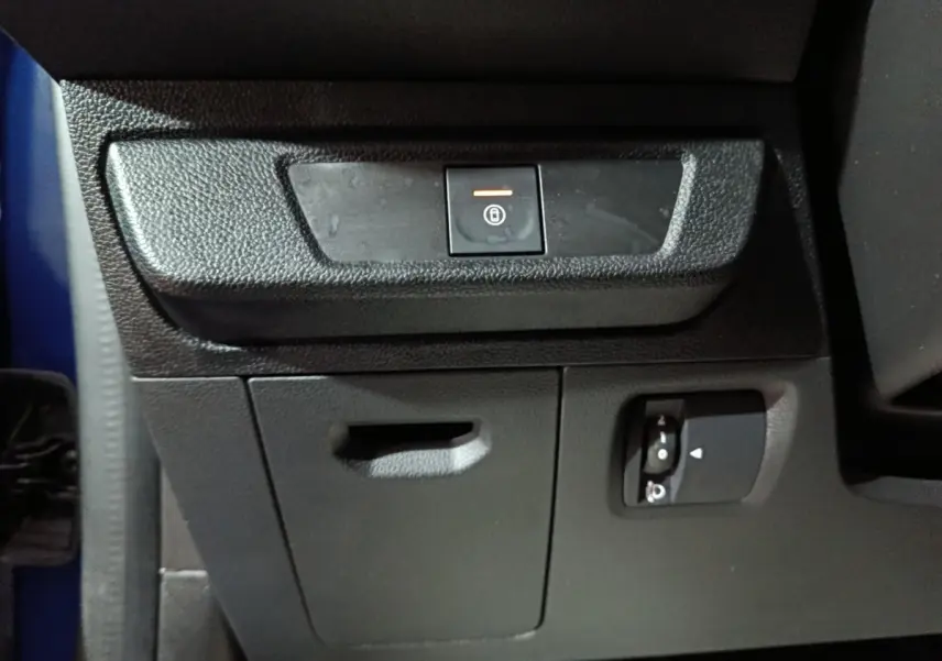 Détail intérieur montrant le bouton de verrouillage central et commandes sur la console inférieure d’une Dacia Sandero bleu.