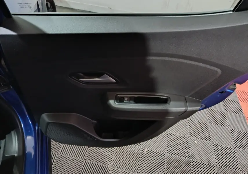 Vue rapprochée de la porte avant gauche bleue de la Dacia Sandero Extreme+ avec poignée intérieure et commande de vitre électrique.