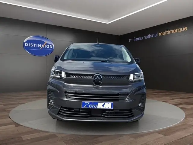 Vue frontale d'un Citroën Jumpy gris foncé 2026 avec phares LED et plaque "Zéro KM" en showroom.