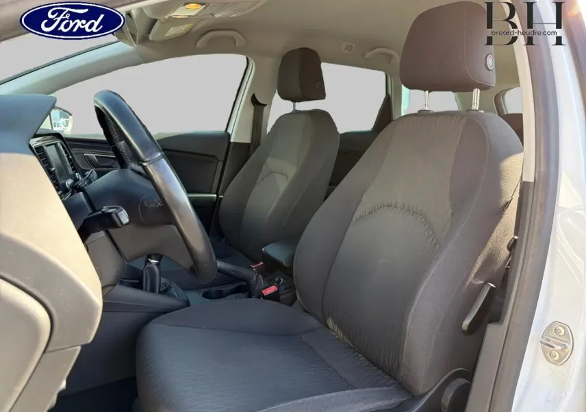 Vue intérieure côté conducteur d'une SEAT LEON ST gris étoile, montrant les sièges avant en tissu noir et le volant multifonction.