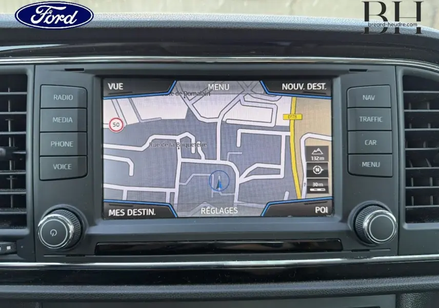 Écran tactile de navigation GPS sur tableau de bord d’une Ford, avec boutons de commande autour et logo Ford visible.