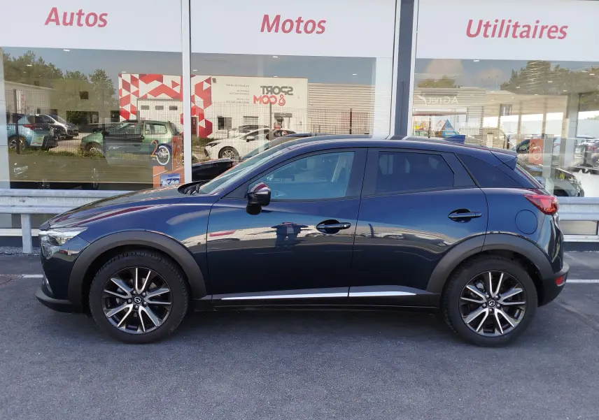 Profil latéral droit d'un Mazda CX-3 2016 bleu Dynamic Blue Mica avec jantes alliage et vitres teintées.