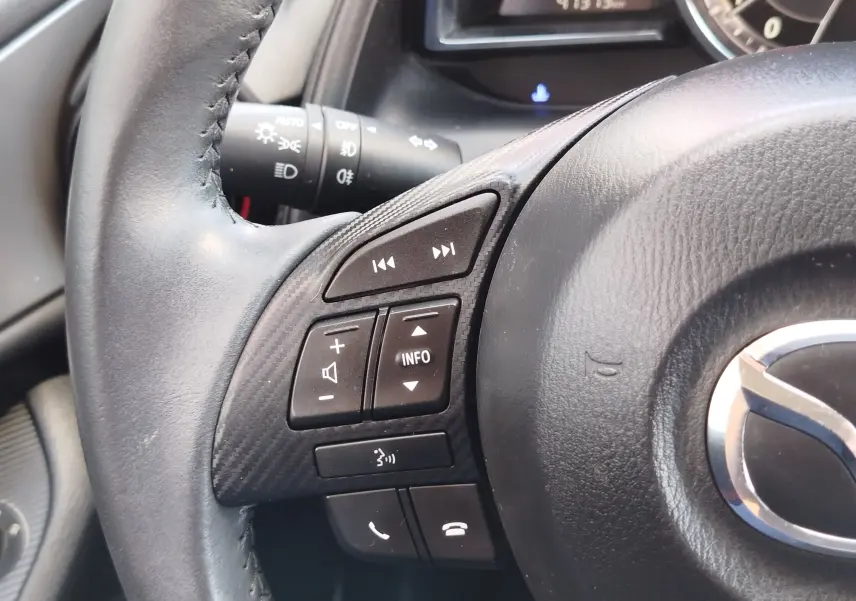 Gros plan sur le volant noir du Mazda CX-3 2016 avec commandes audio et téléphone intégrées.