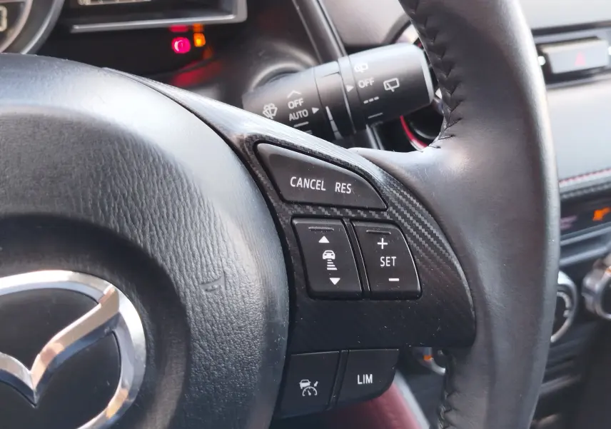 Gros plan sur le volant en cuir noir du Mazda CX-3 2016 avec commandes de régulateur de vitesse et finition carbone.