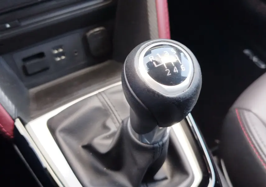 Gros plan sur le levier de vitesses manuel noir du Mazda CX-3 2016, avec coutures rouges visibles sur le siège adjacent.