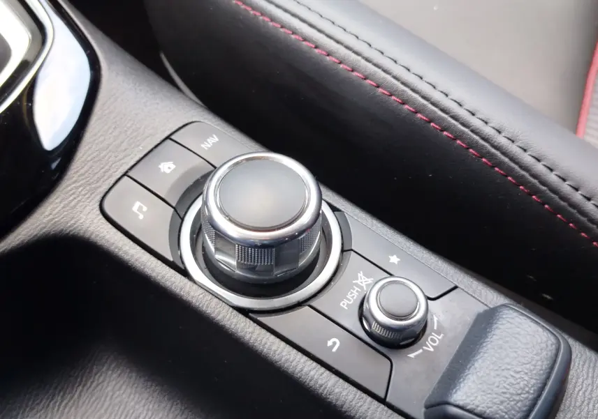 Gros plan sur la molette de commande multimédia et le volant en cuir noir avec surpiqûres rouges du Mazda CX-3 2016.