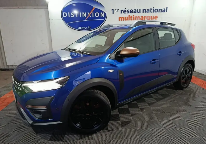 Dacia Sandero Extreme+ TCe 110 2024 bleu, vue 3/4 avant droit, rétroviseurs bronze et jantes noires distinctives.