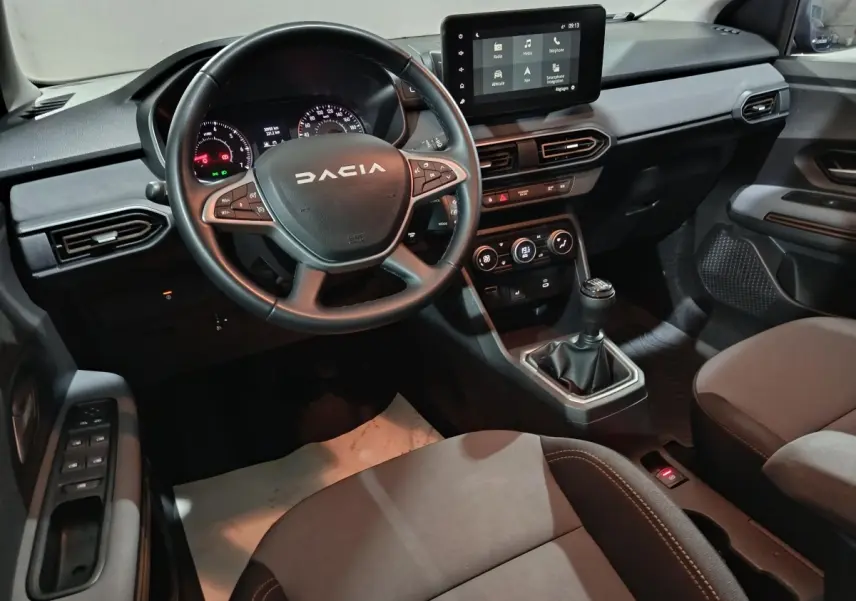 Vue intérieure avant droite du tableau de bord de la Dacia Sandero 2024 avec volant cuir multifonctions et écran tactile central.