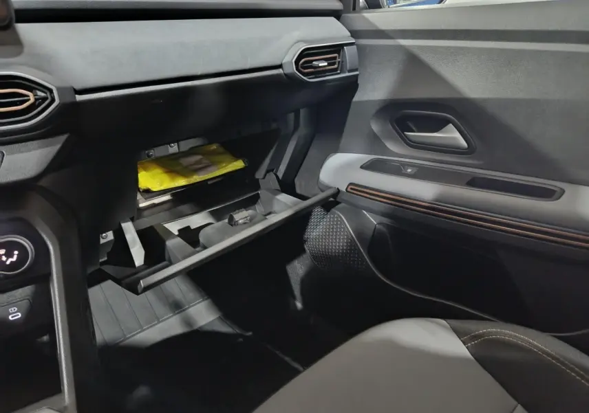 Vue intérieure côté passager de la Dacia Sandero Extreme+ 2024, boîte à gants ouverte avec gilet jaune visible.
