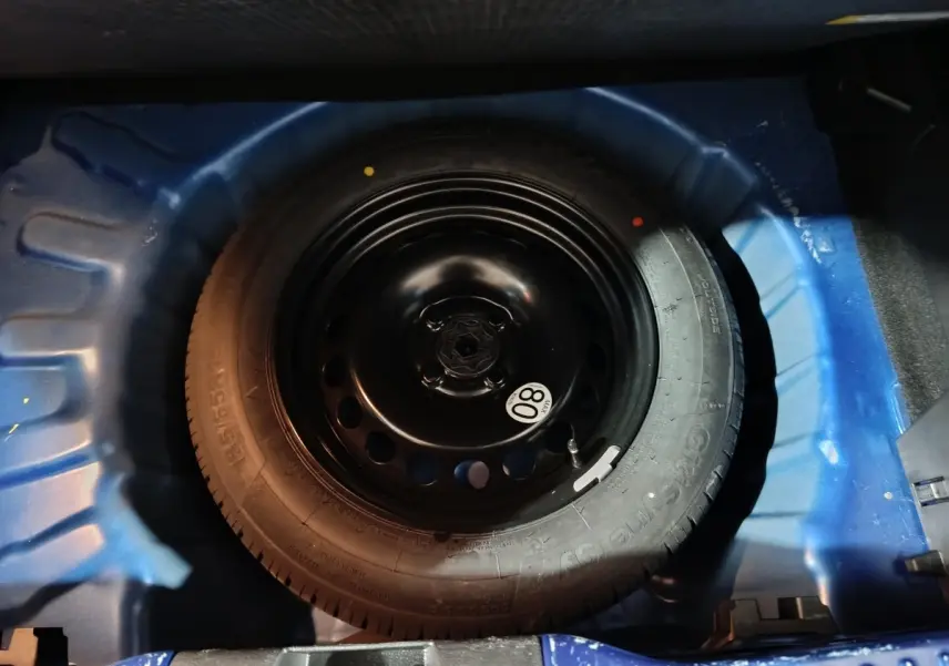 Roue de secours galette noire dans le coffre bleu d'une Dacia Sandero Extreme+ TCe 110 2024.