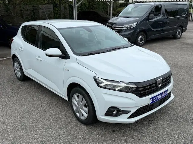 Vue 3/4 avant d'une Dacia Sandero 2023 blanc glacier avec calandre noire et feux LED, stationnée sur un parking.